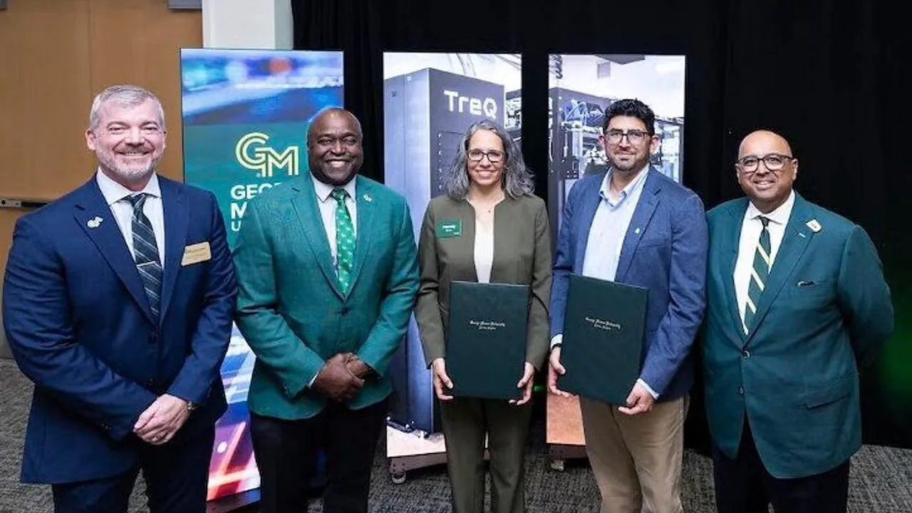 Five people stand before display banners, with two holding presentation folders.