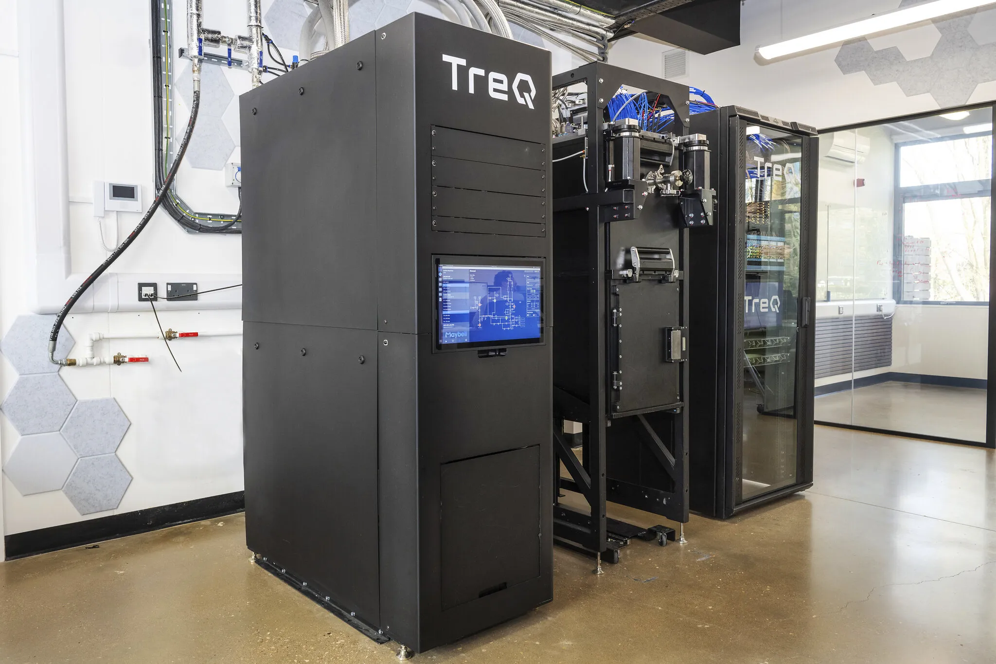 Large black industrial machine with control screen and glass enclosure in a laboratory.