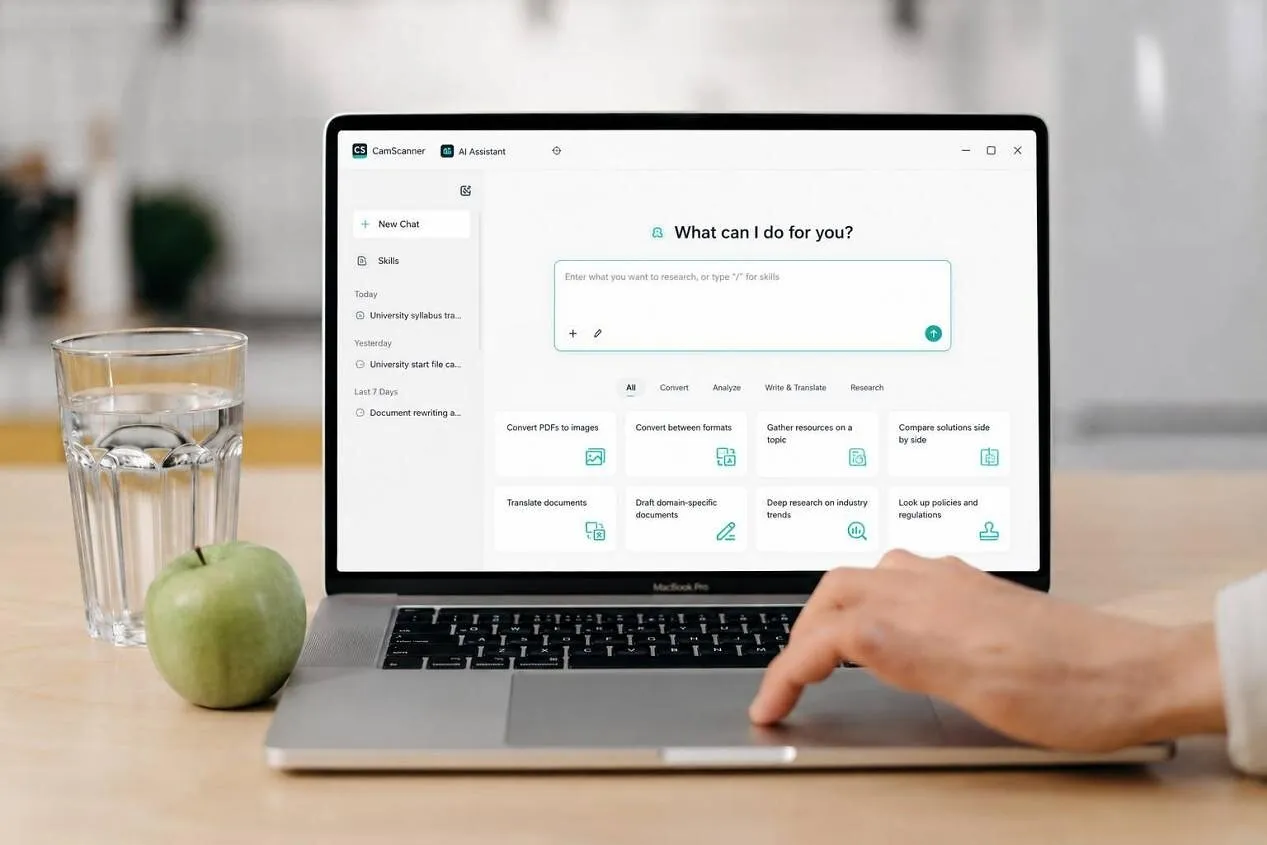 A laptop displaying an AI assistant interface beside a glass of water and a green apple.