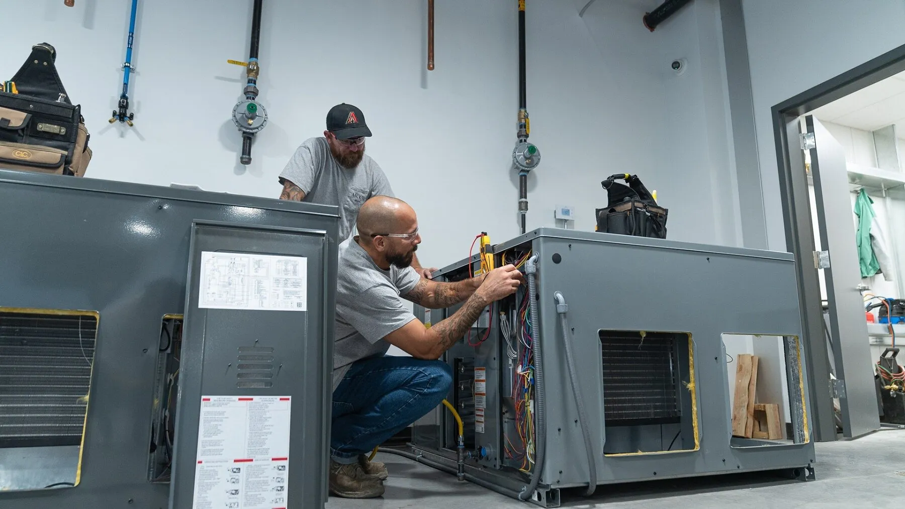 Two technicians work on HVAC units in a classroom workshop.