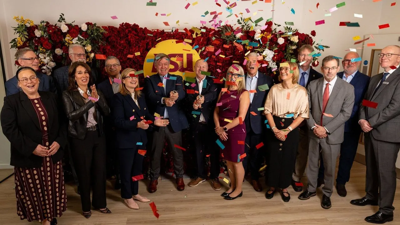 A group celebrates beneath falling confetti in front of a flower-covered ASU sign.