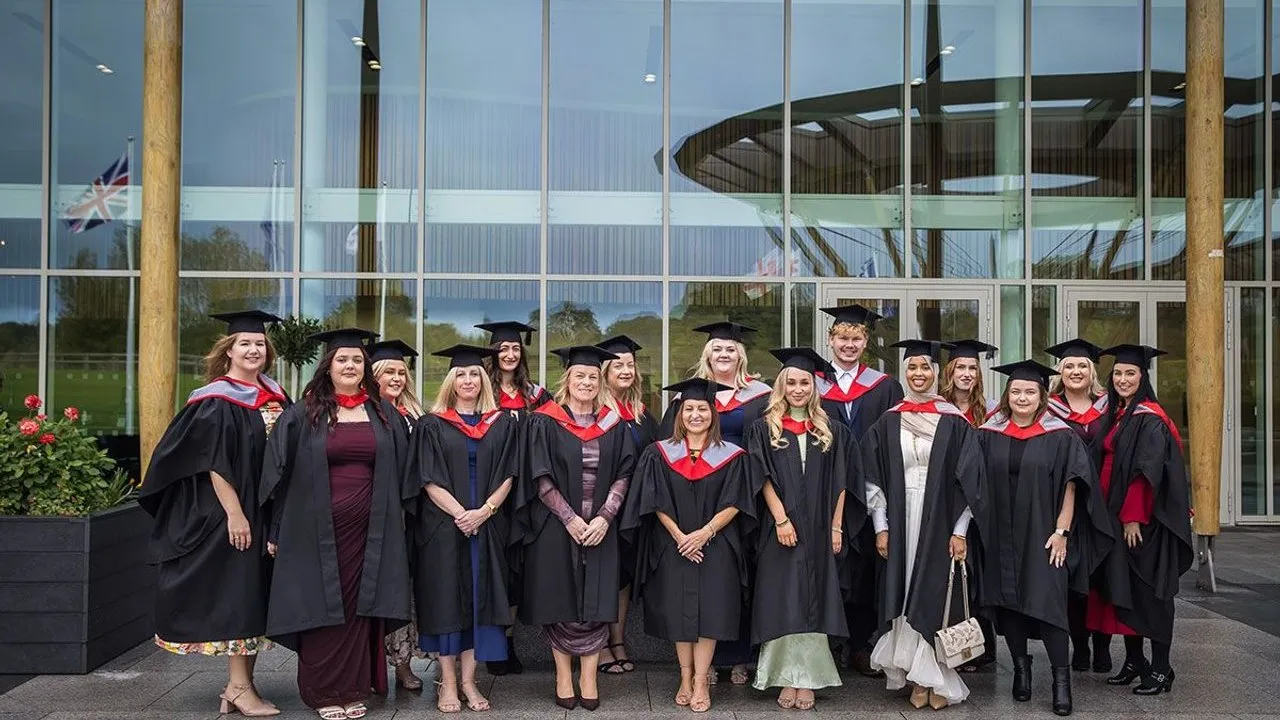 A group of graduates in caps and gowns standing outside a glass-fronted building.