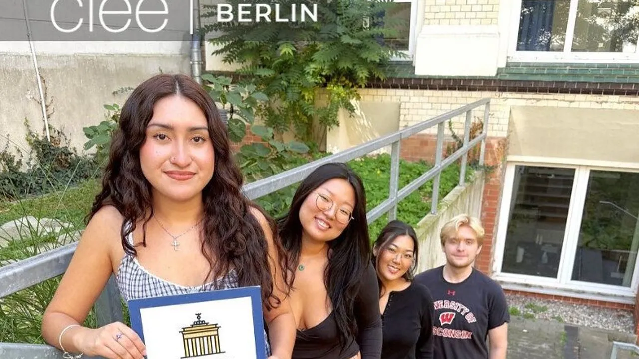 Four students stand outside CIEE Berlin, with one holding a Brandenburg Gate illustration.