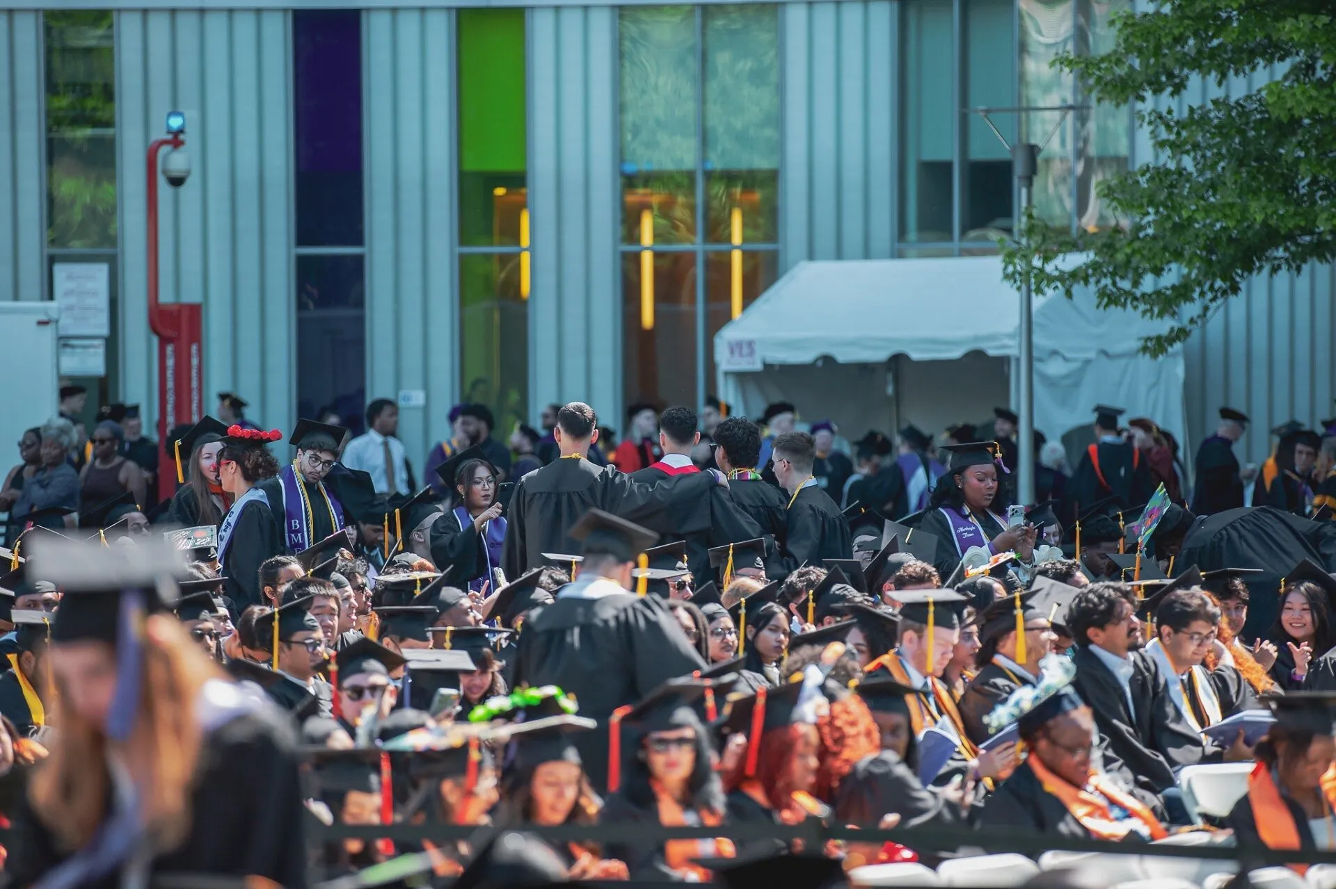 Graduates in caps and gowns gathered outside a campus building.