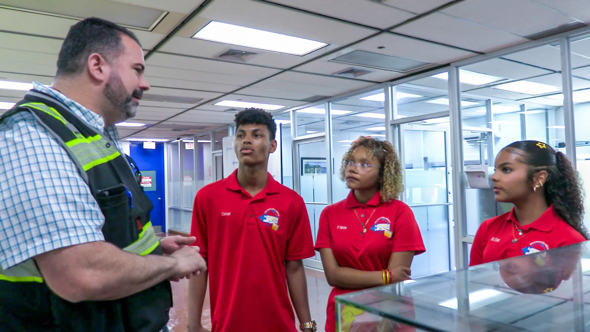 A safety officer speaks with three students in red Crowley Workforce shirts.