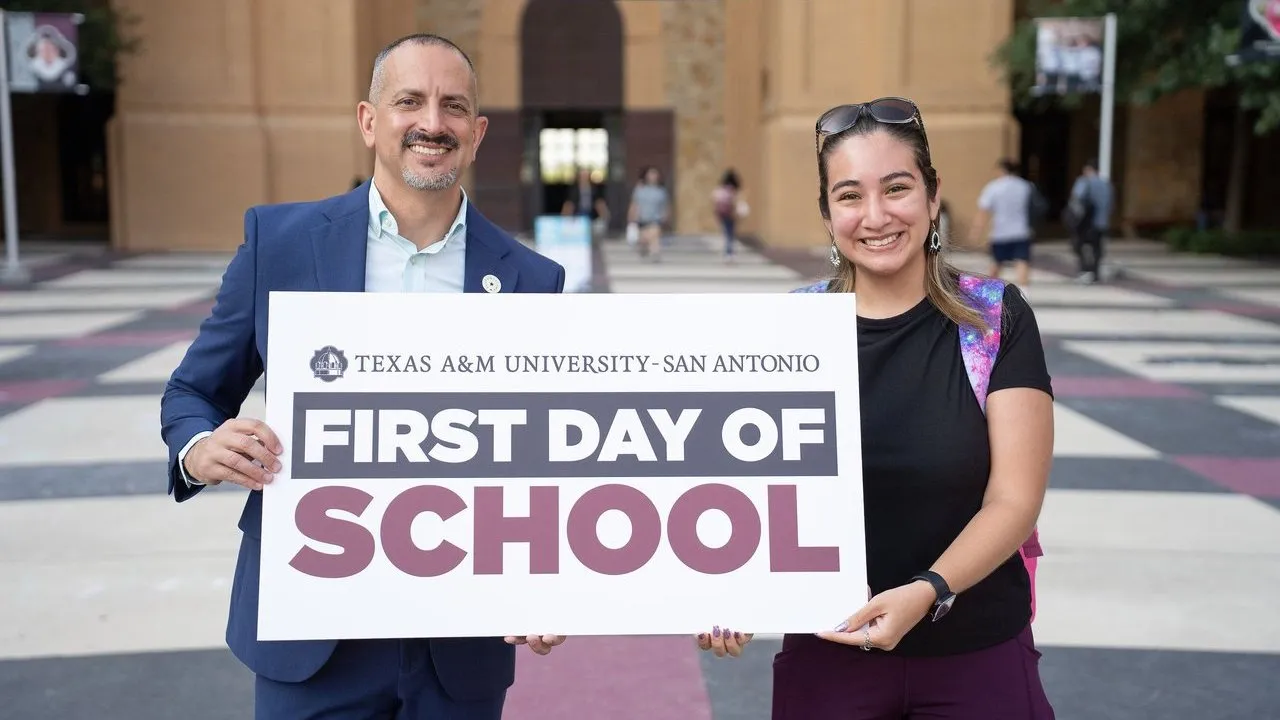 Two people hold a Texas A&M University–San Antonio “First Day of School” sign outside a campus building.