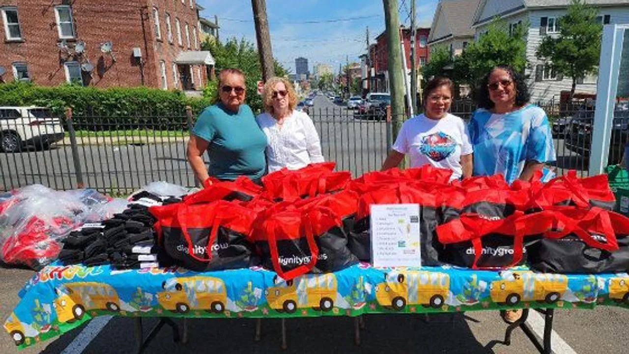 Four women stand behind a table of red bags and supplies at a school event.