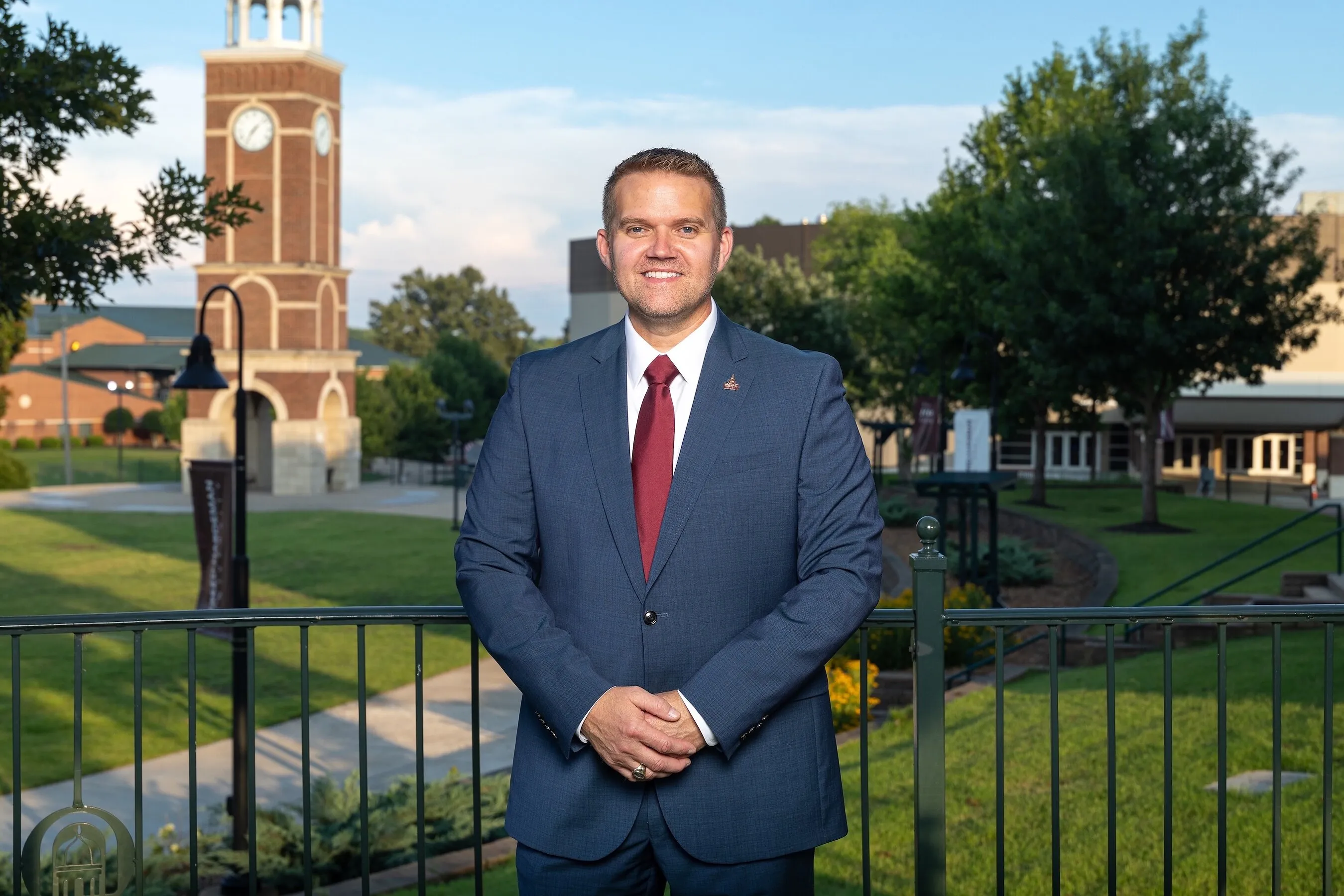 Dr Keith Harris in a blue suit standing outside a brick clock tower.