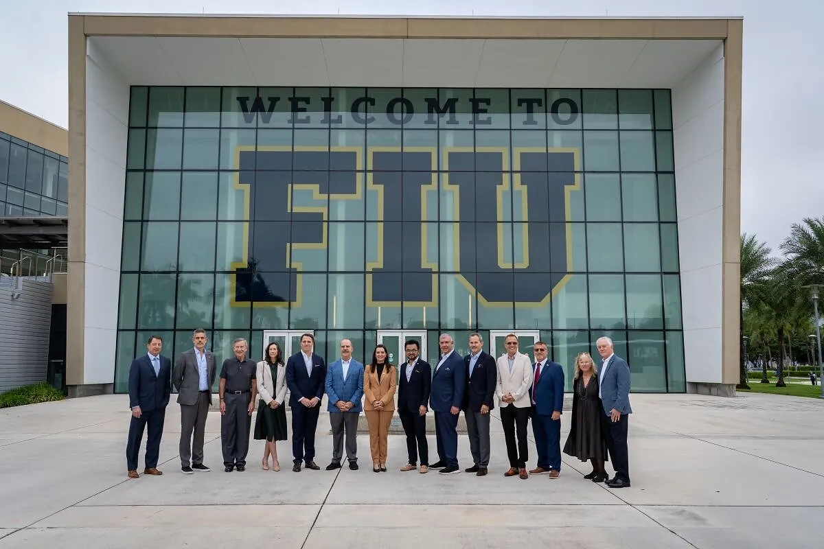A group of executives stands outside Florida International University beneath a large FIU sign.