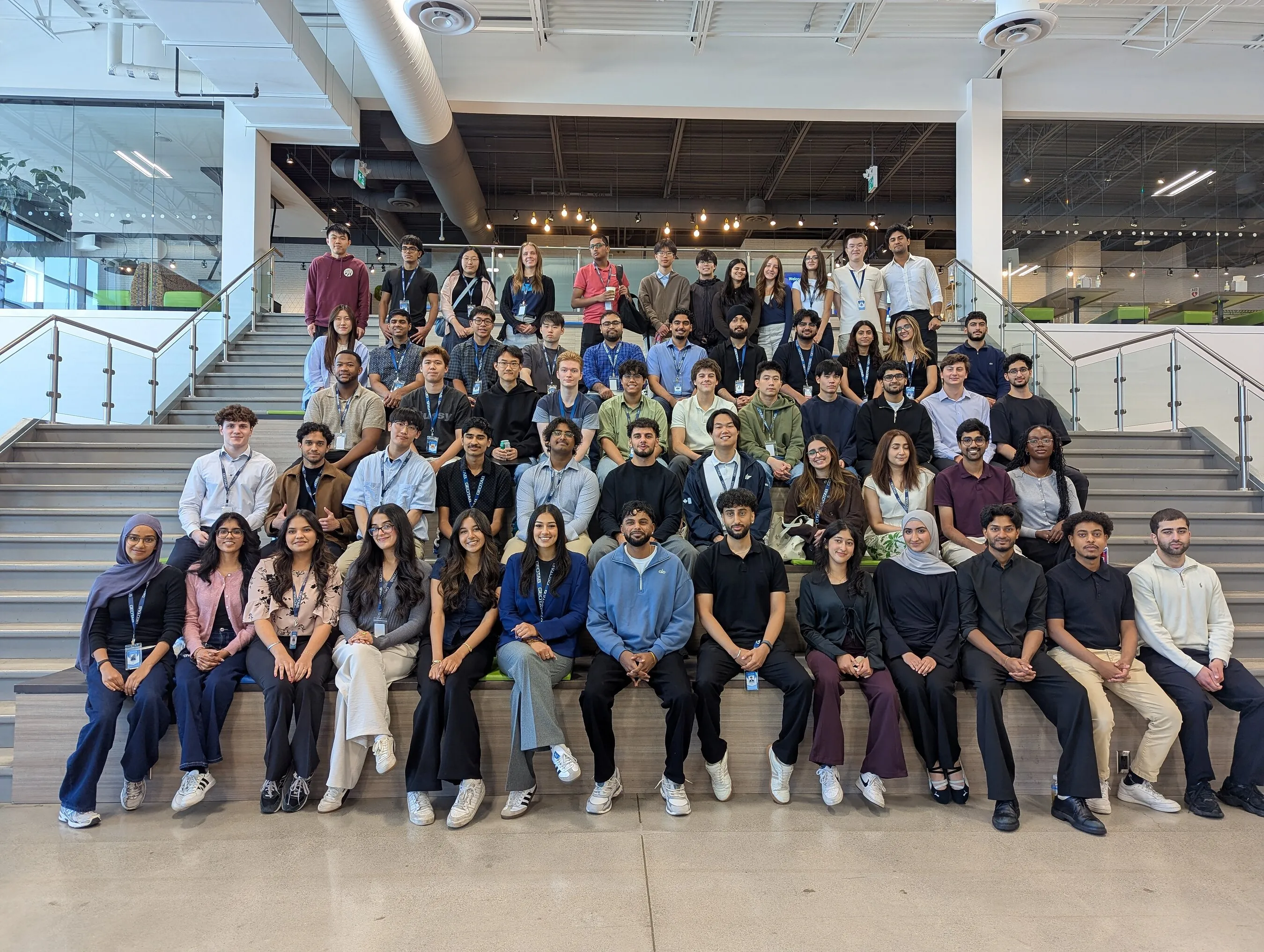 A large group of young adults wearing lanyards pose on an indoor staircase.