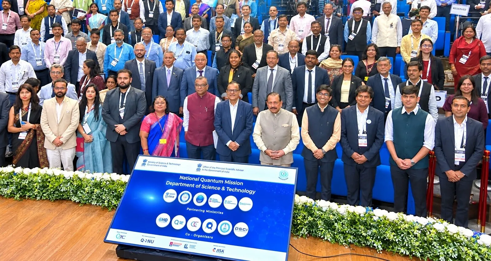 Large group of conference attendees posing behind a National Quantum Mission sign.
