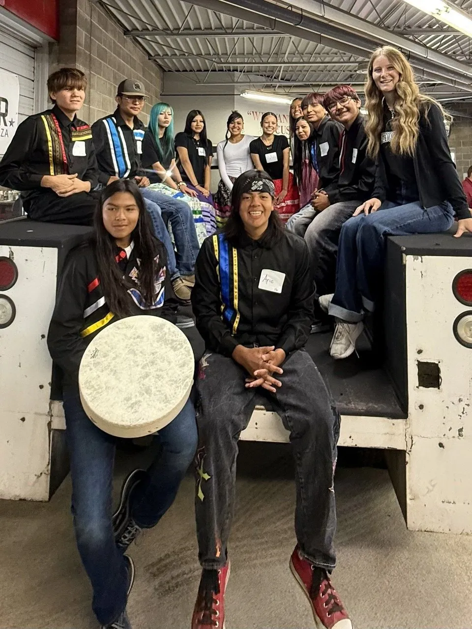 A group of young people in traditional clothing sitting on the back of a white truck