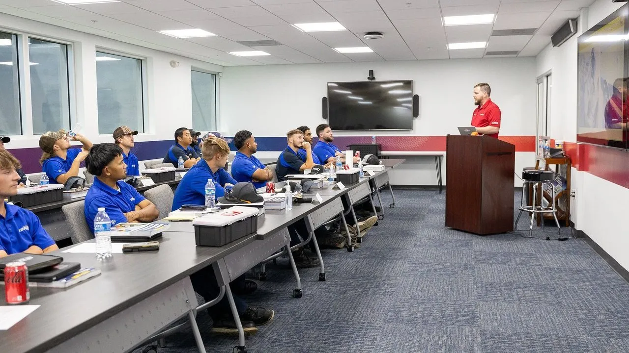 Technicians in blue uniforms attend classroom instruction led by an instructor.