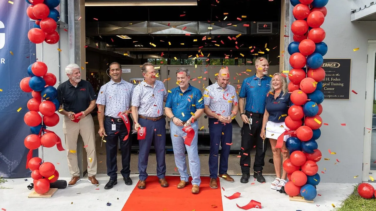 Seven people cut a ribbon beneath red and blue balloon arches.