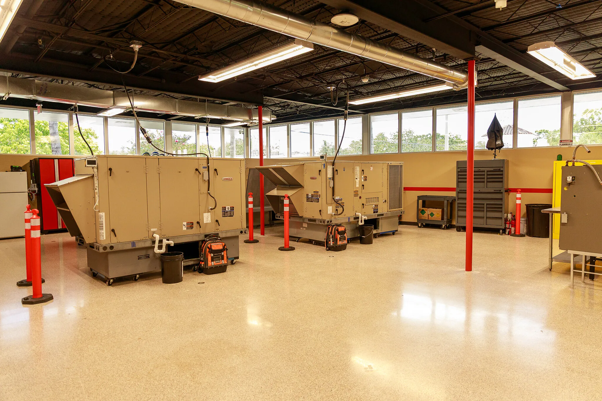 Industrial HVAC training room with Lennox air-handling units, red posts, and tools.