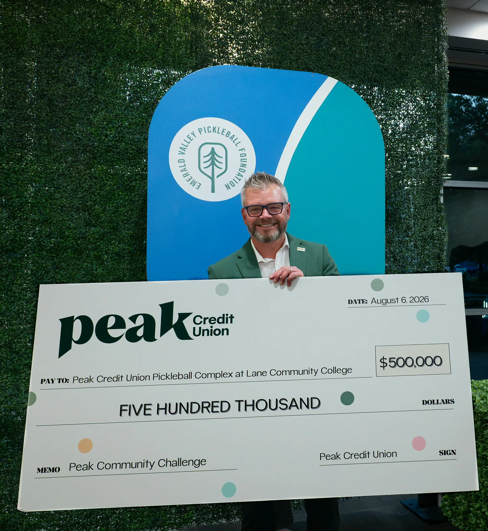 Man holds a $500,000 Peak Credit Union cheque for a pickleball complex.