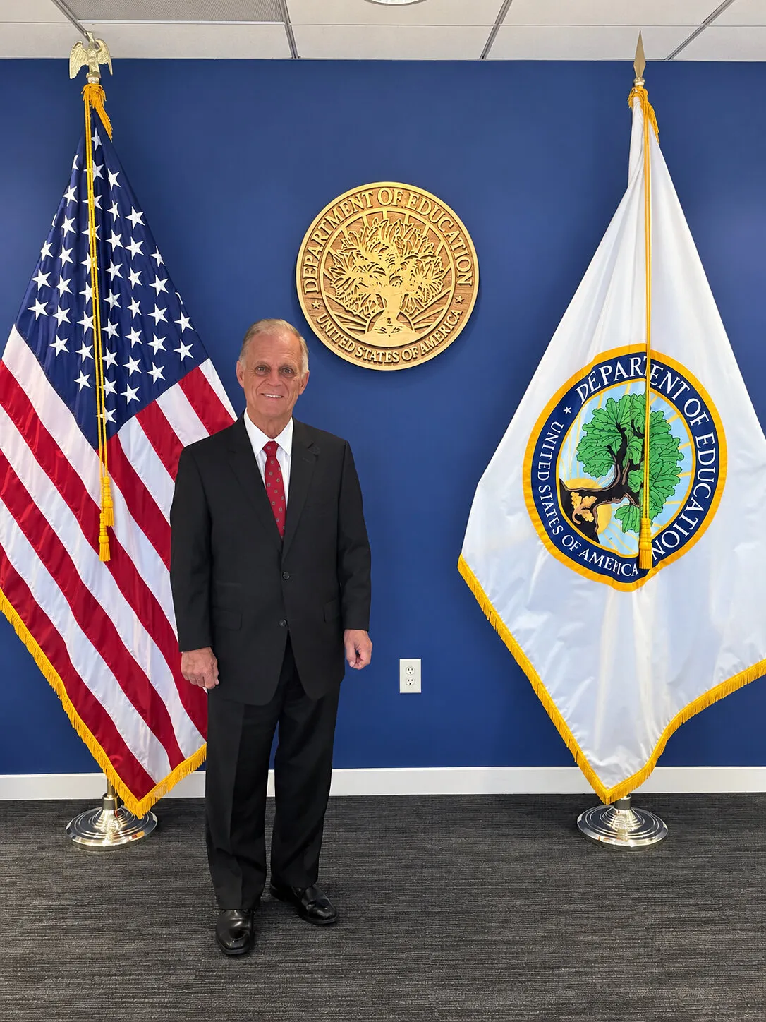 Terrence Terry Giroux standing between US and Department of Education flags beneath an Education Department seal.