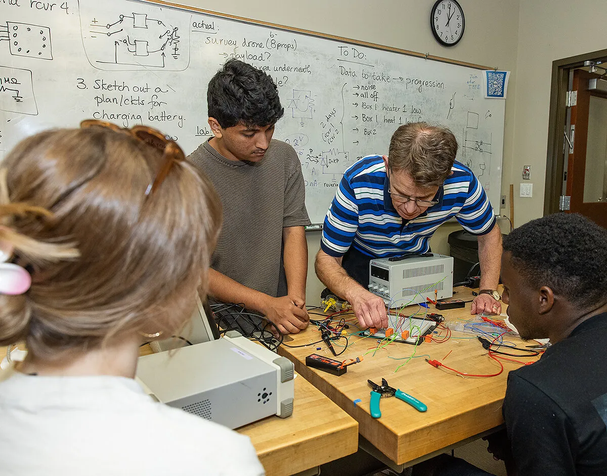 Students and an instructor work with electronics on a lab bench.