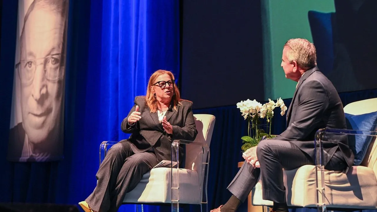 Cori Close and Brian Cornell talk onstage beside a large portrait banner of John Wooden.