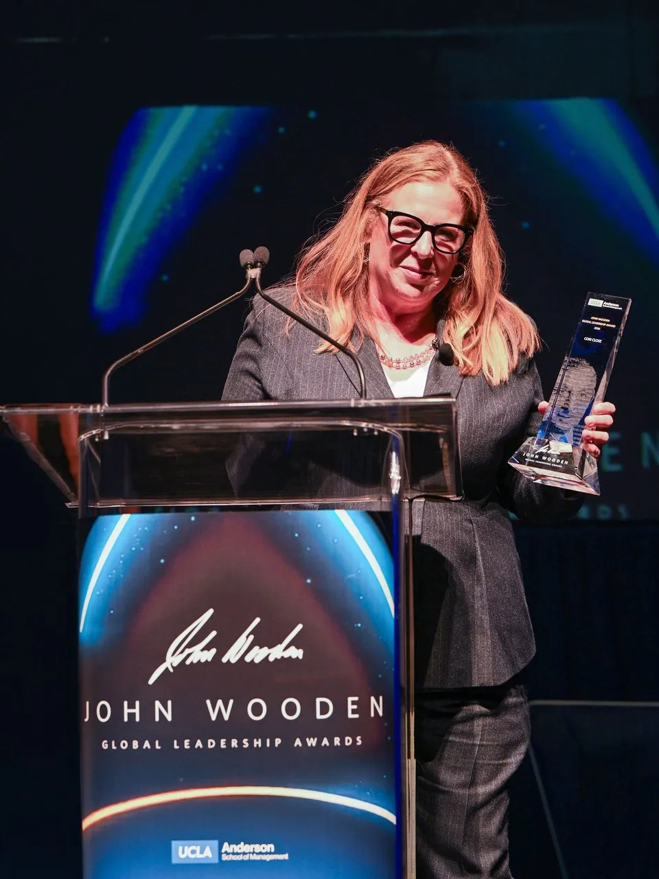 Cori Close holds her award at a John Wooden Global Leadership Awards podium.