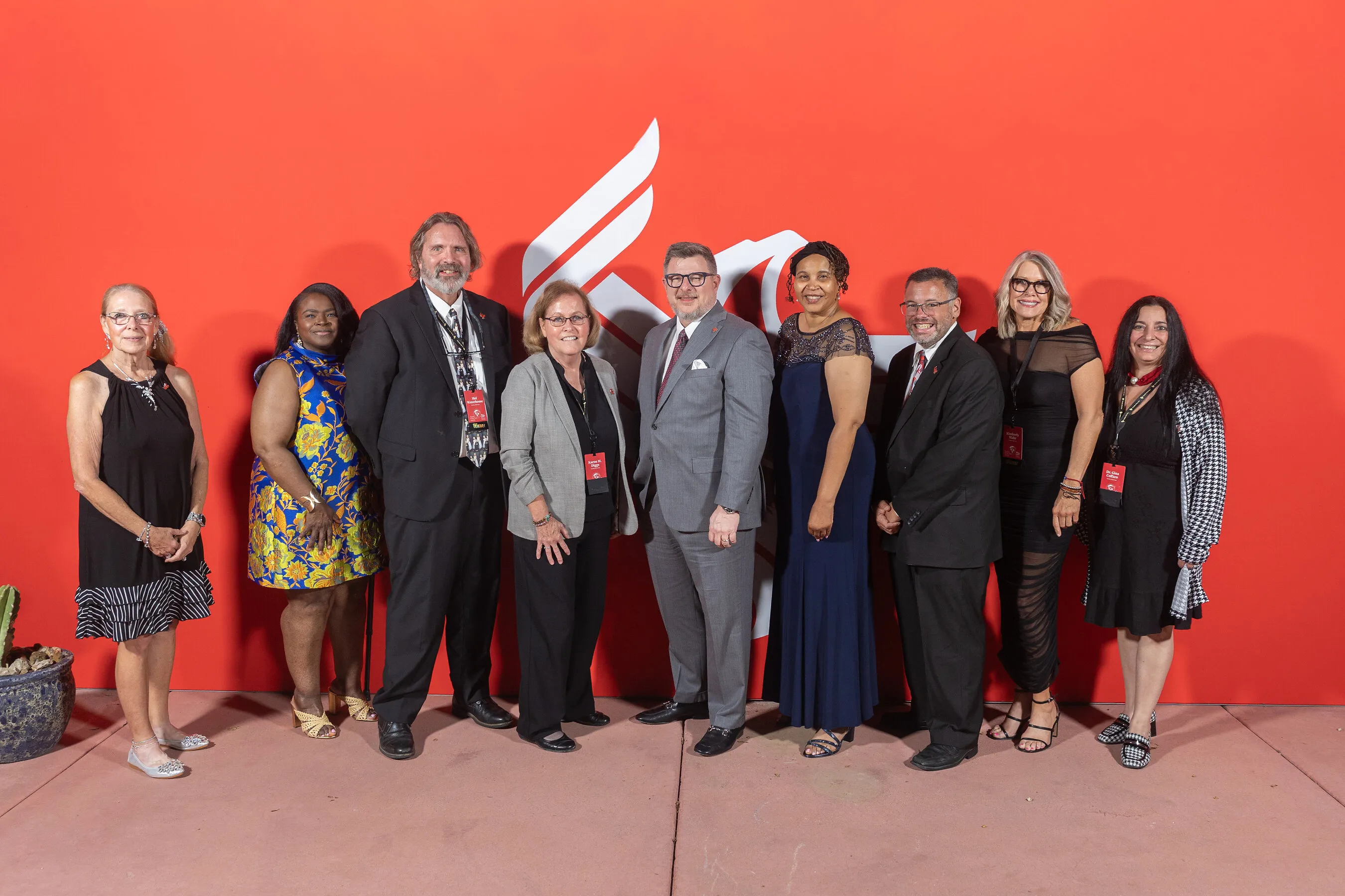 Nine Faculty of the Year recipients pose before a red University of Phoenix backdrop.