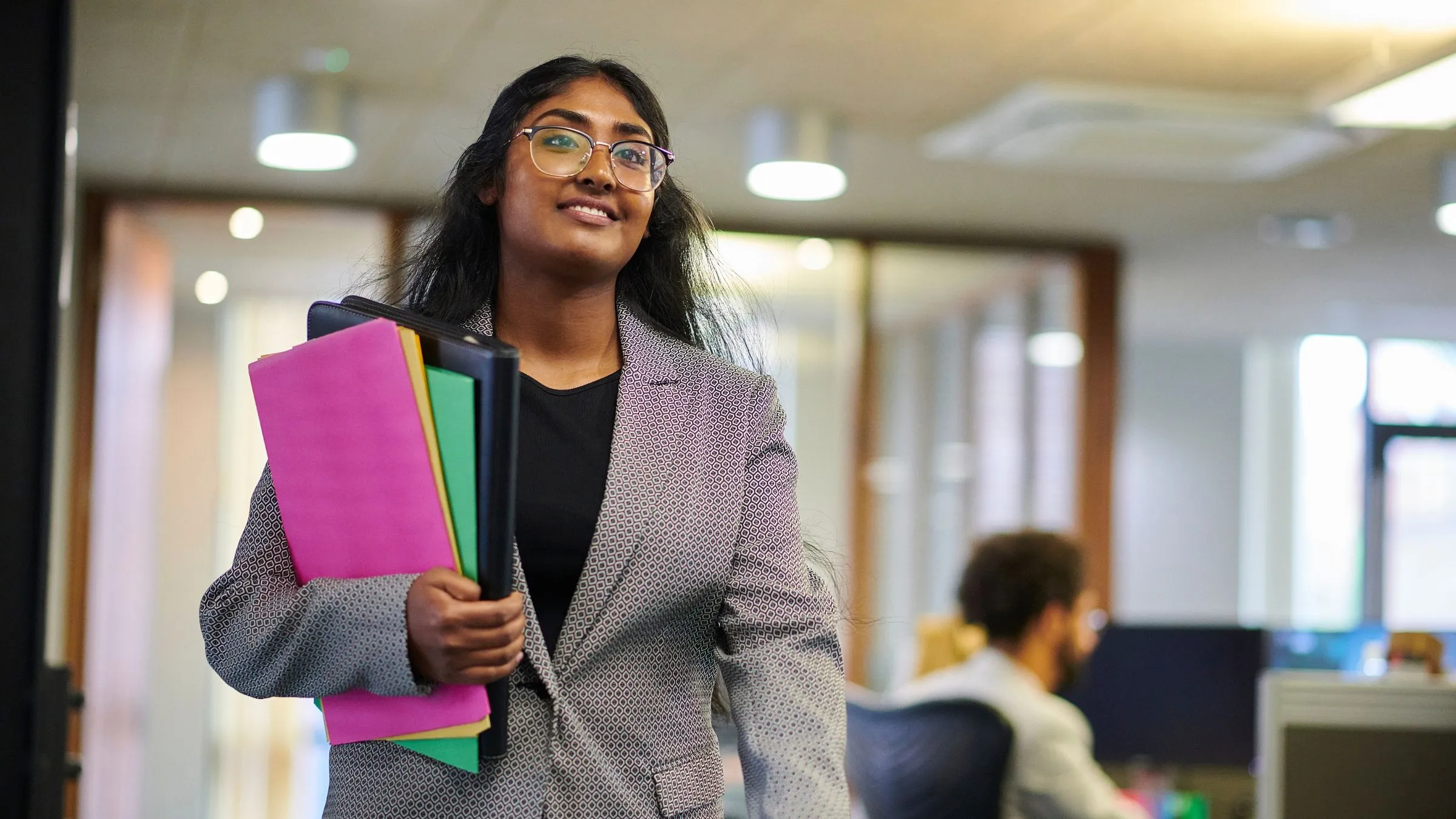 A young professional walking through an office holding folders