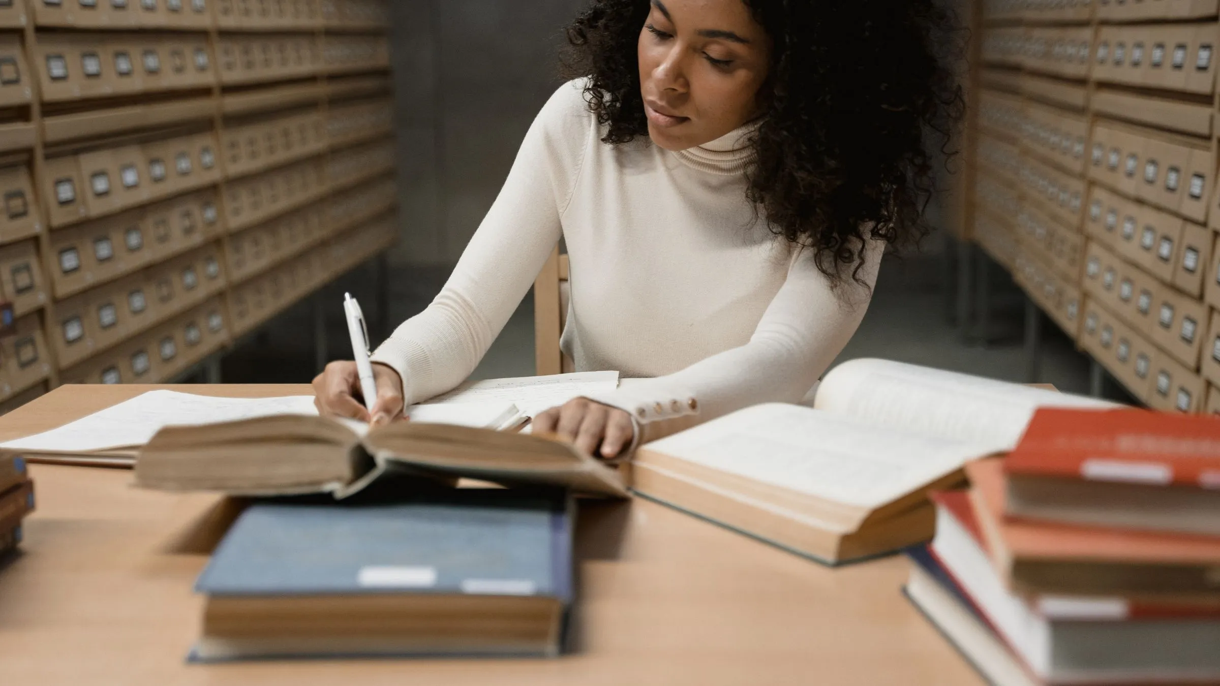 A student writing by hand among open books in a library