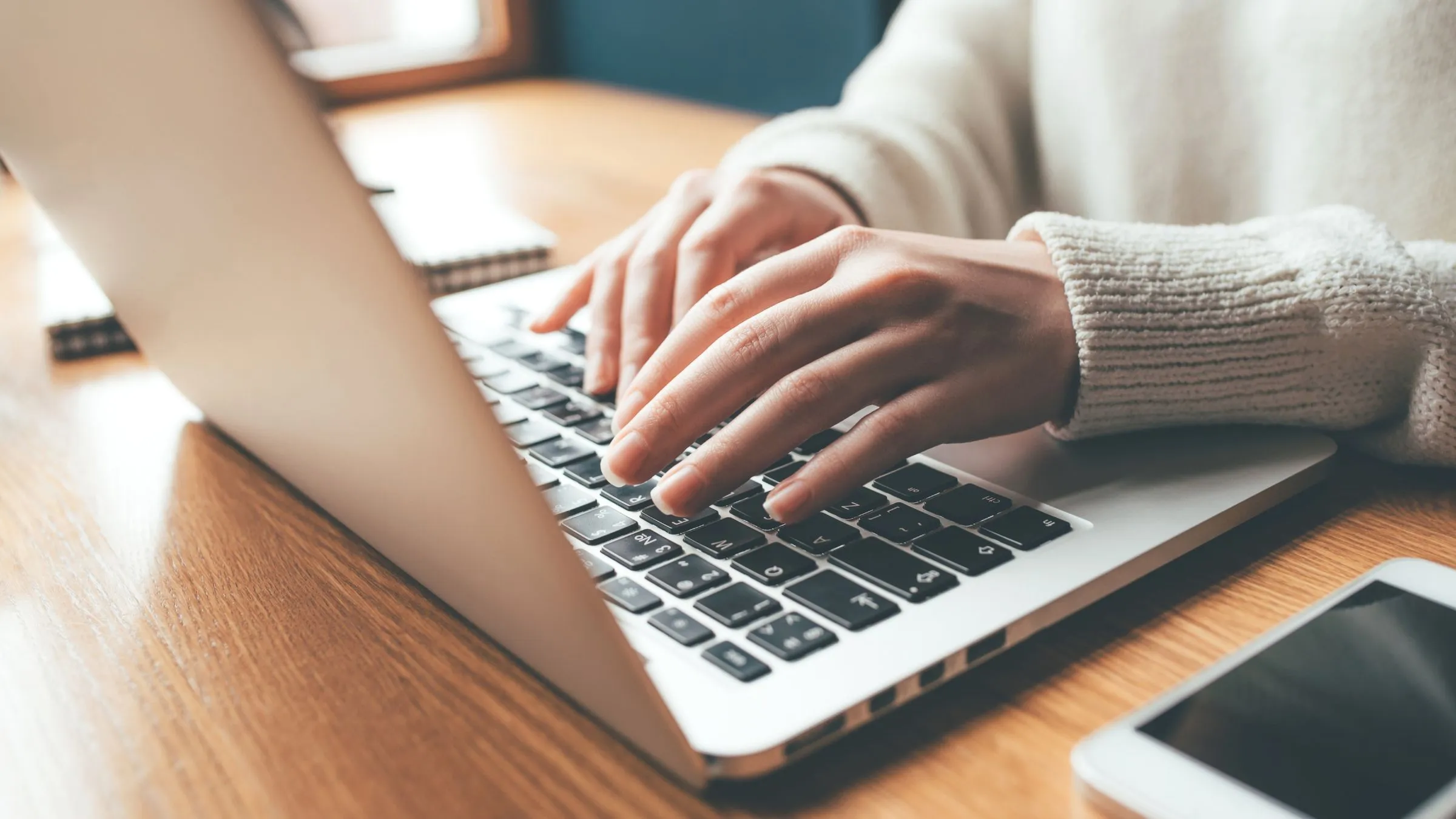 Close-up of hands typing on a laptop keyboard at a wooden desk