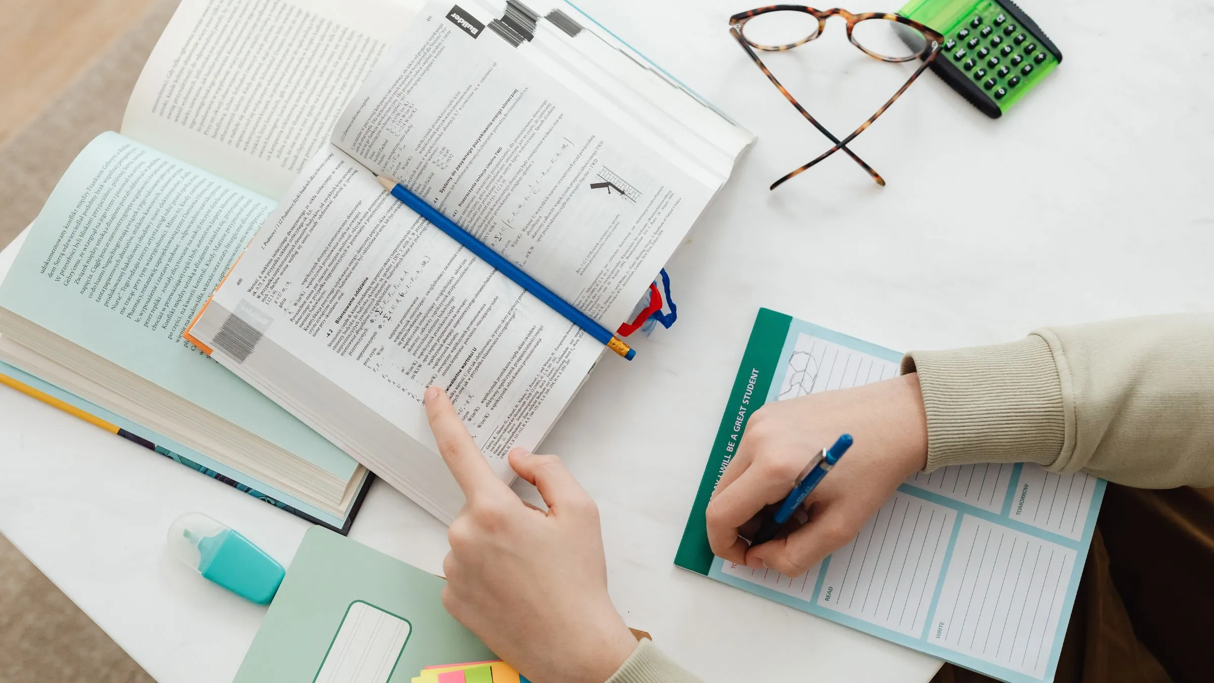 A reader following a printed text with one finger and taking notes with a pen