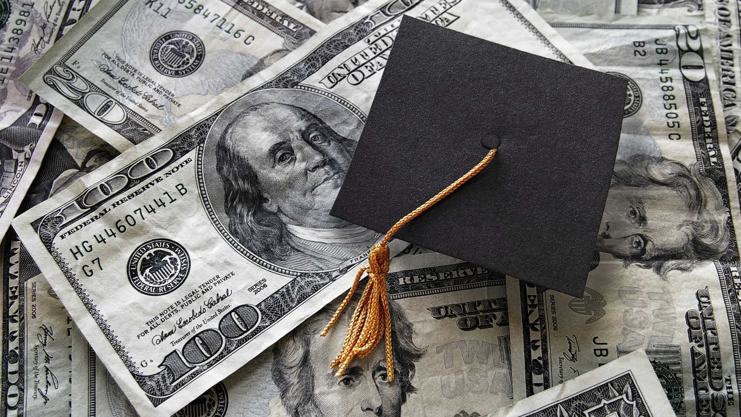A graduation cap lying on a spread of hundred-dollar bills
